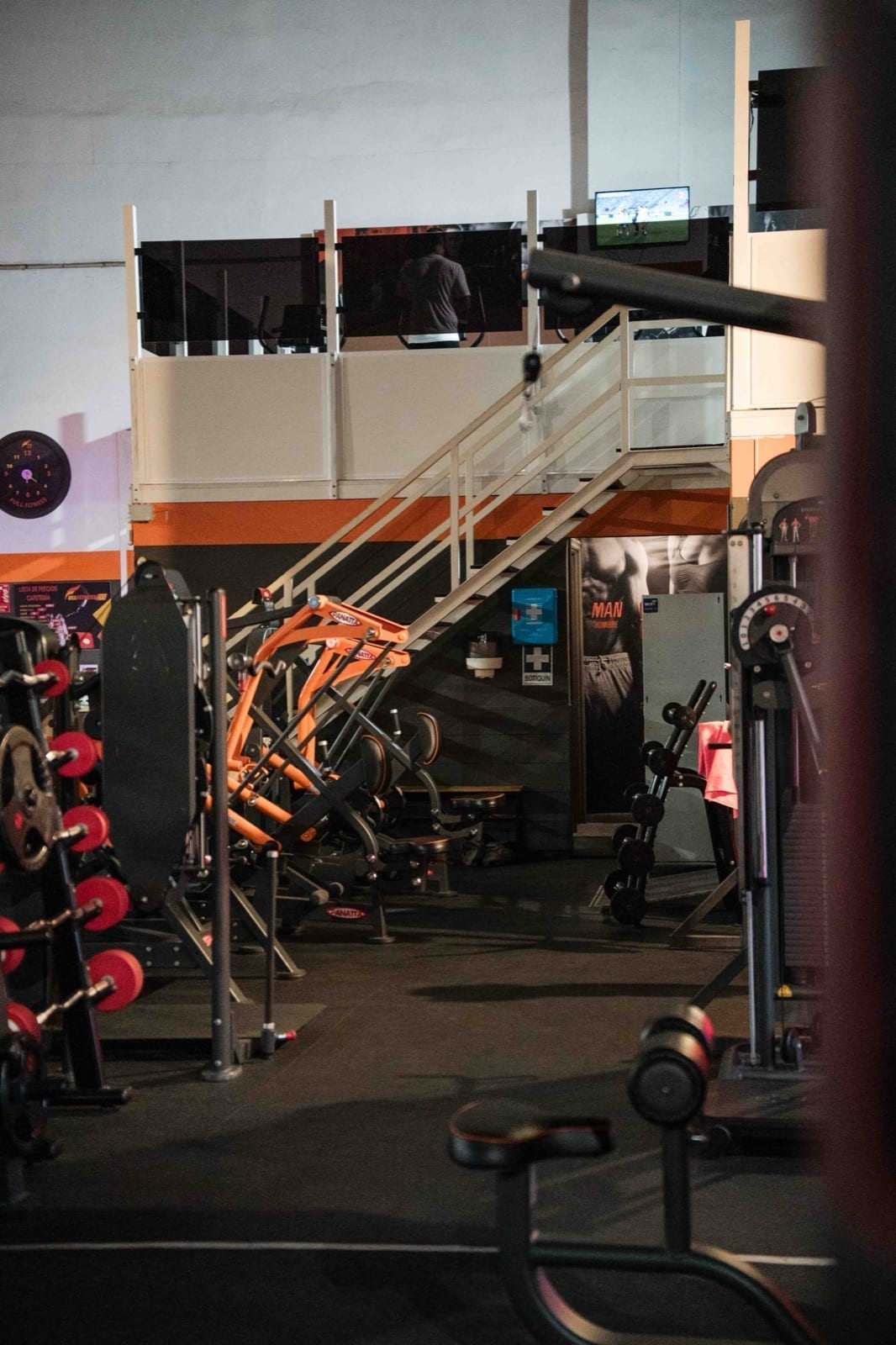 Sala principal: Vista de la nave con mezzanine y máquinas en naranja corporativo. Gimnasio FullFitness77 en Adeje, Tenerife Sur.